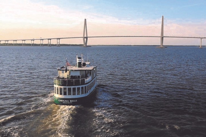 Boat on water beneath a large bridge under a clear sky.