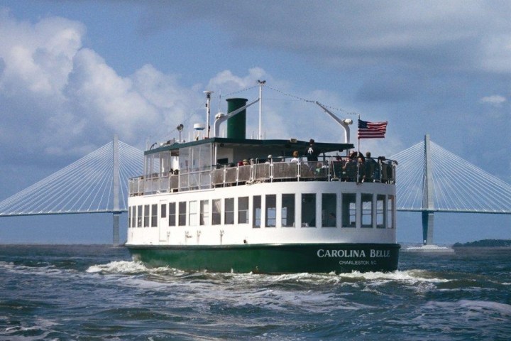 A ferry named Carolina Belle with passengers, American flag, bridge in background.