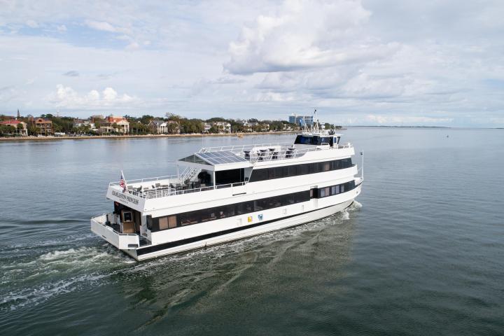 White ferry boat on calm water near a shoreline with buildings.