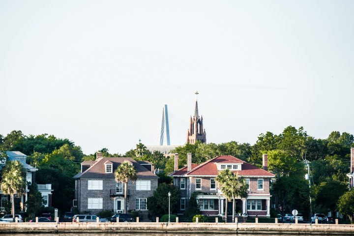 Historic houses with a church and suspension bridge in the background.