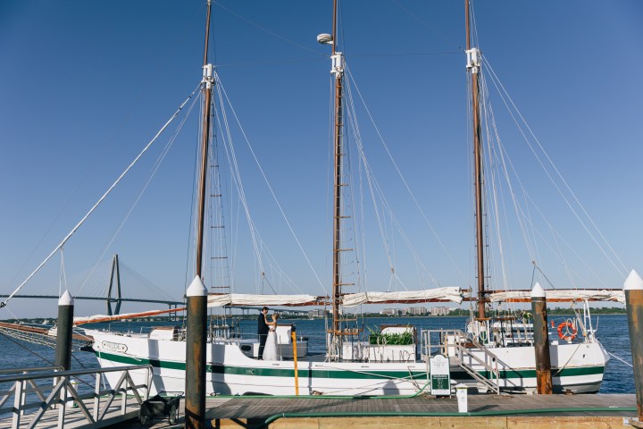 Two-masted sailboat docked at a pier with a blue sky background.