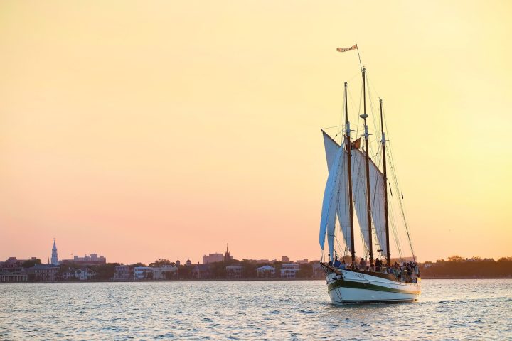 Sailing ship on water at sunset with distant city skyline.