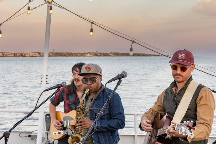 Band playing on a boat during sunset with string lights overhead.