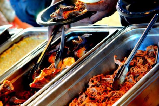 Person serving barbecue meat from trays at a buffet.