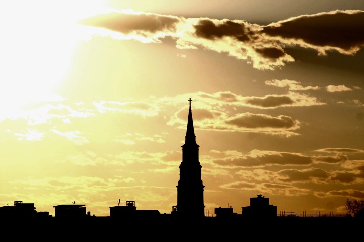 Silhouette of a church steeple against a golden sunset sky with scattered clouds.
