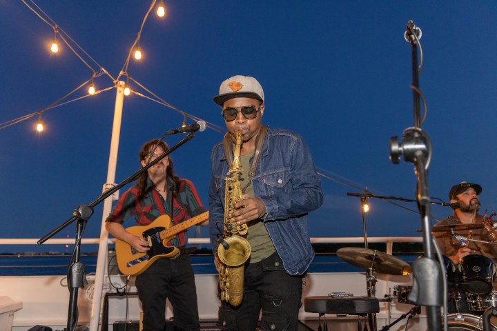 Musicians performing on a deck at night, with lights overhead.