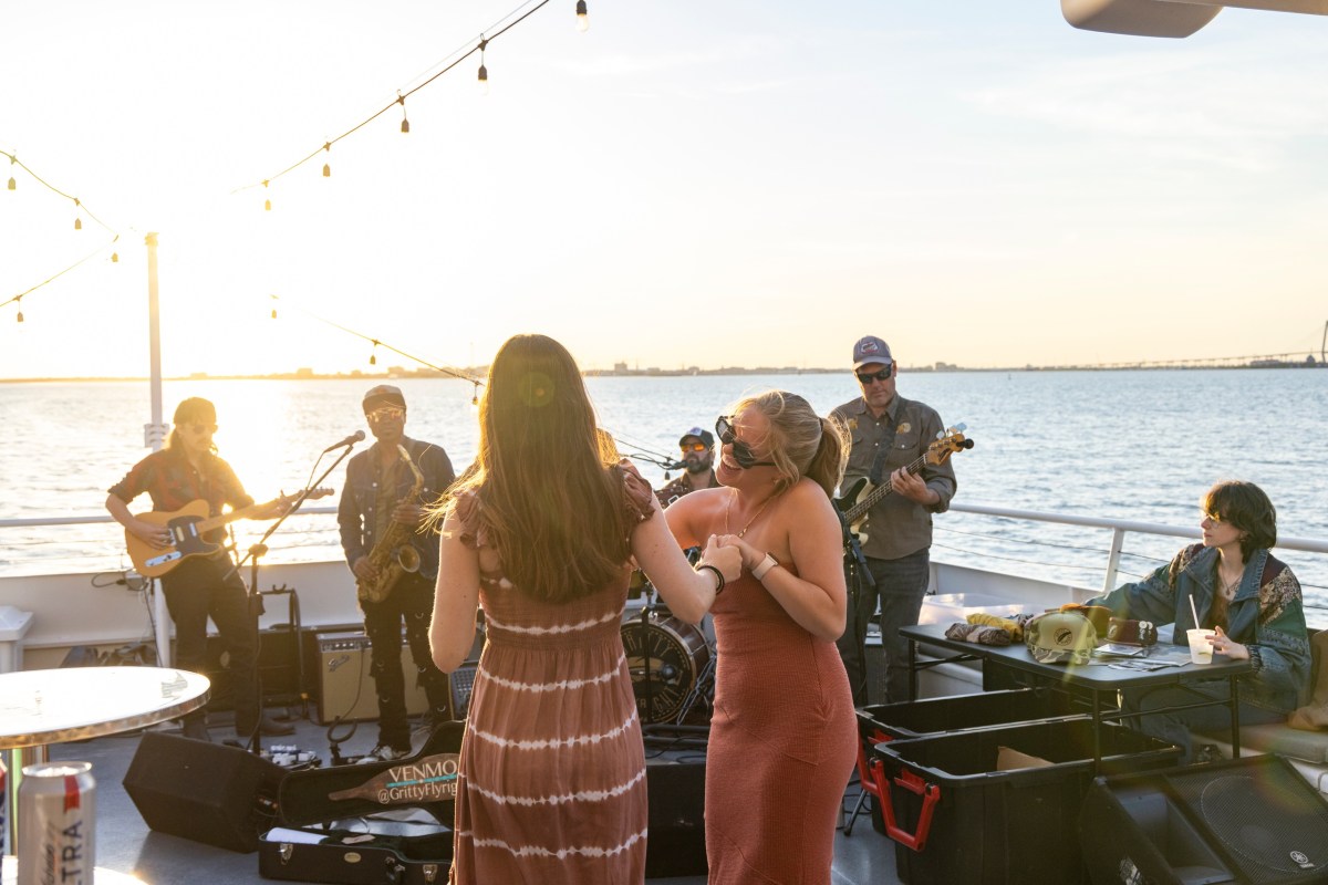 People dancing on a boat with a band playing at sunset.