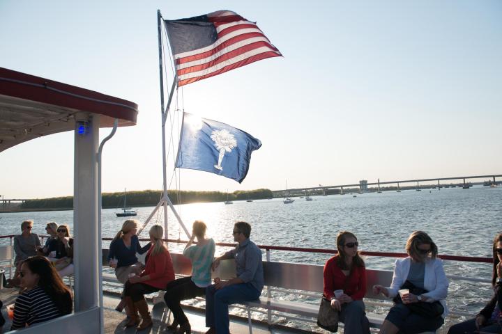 People sitting on a boat deck with American and state flags, river view in background.