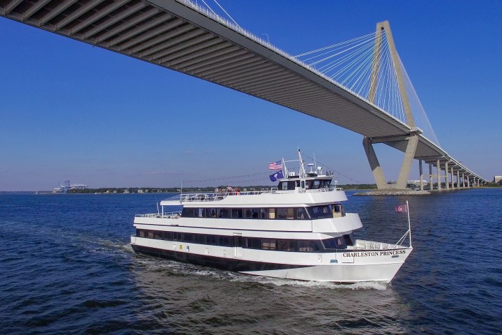 Tour boat sails under large cable-stayed bridge over a blue river.