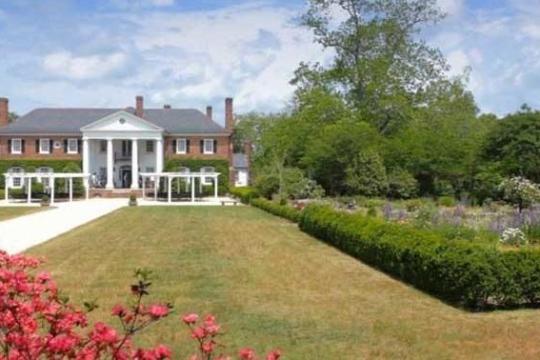 Large brick house with columns, garden, and pathway under a blue sky.