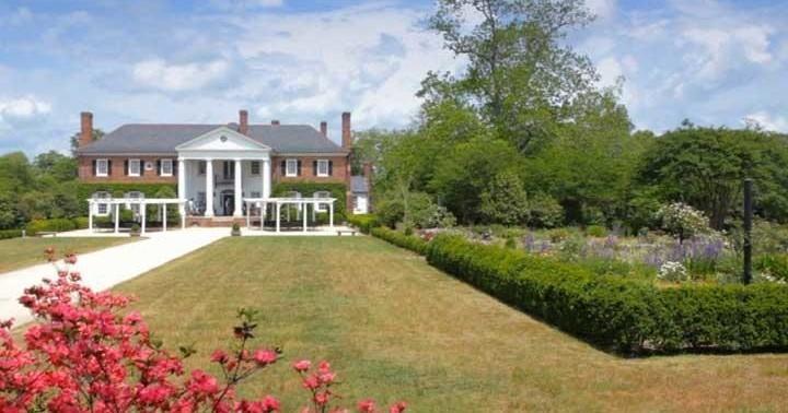 Large brick house with columns, garden, and pathway under a blue sky.