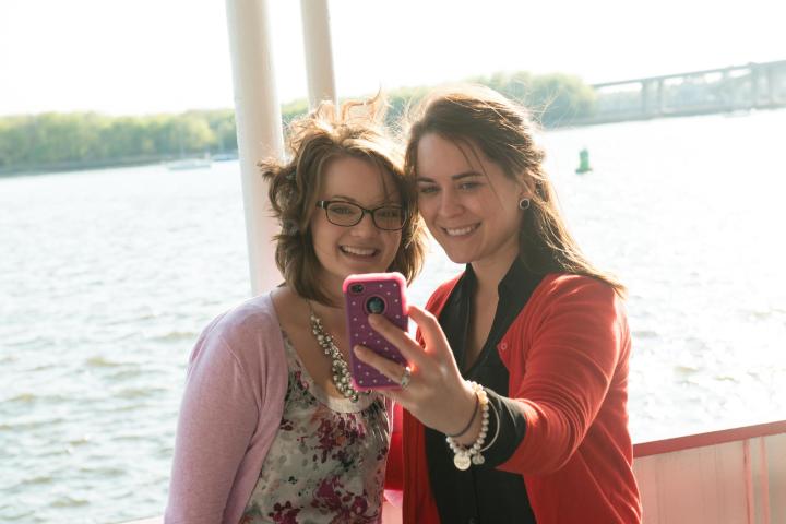 Two women smiling while taking a selfie on a boat near water.