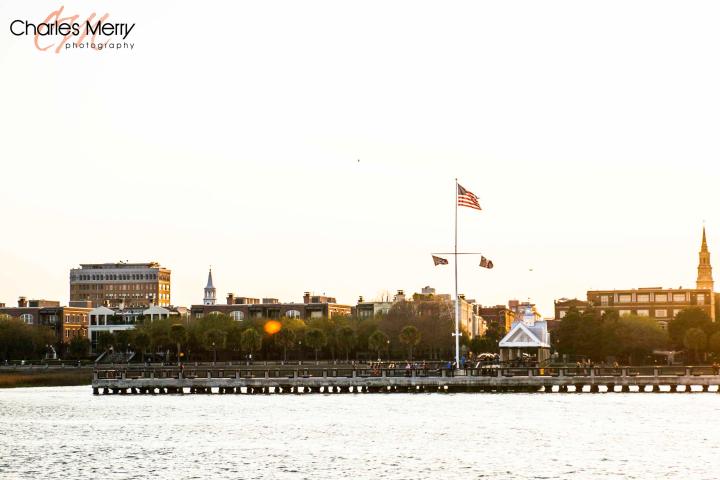 Waterfront scene with buildings, pier, and flags at sunset.