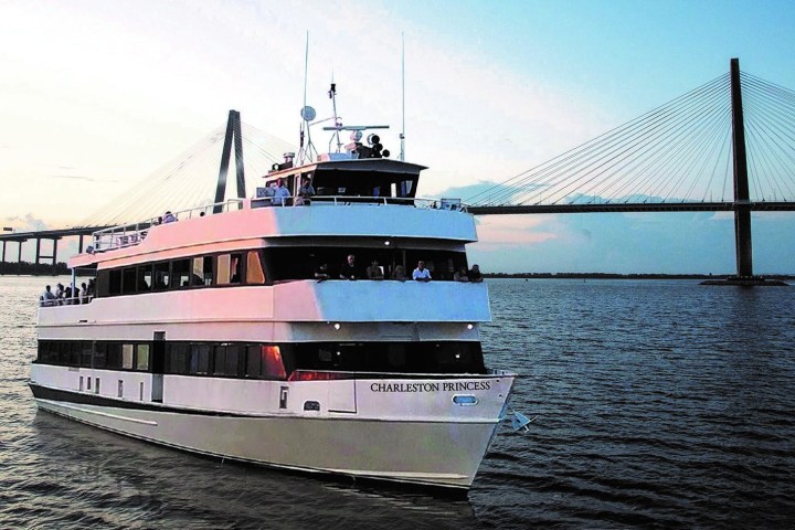 White yacht cruising near a suspension bridge at sunset.
