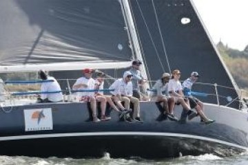 Sailboat with crew sitting on edge, sailing on water.