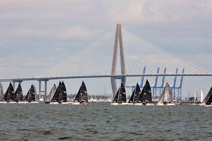 Several sailboats on water with a large bridge in the background.