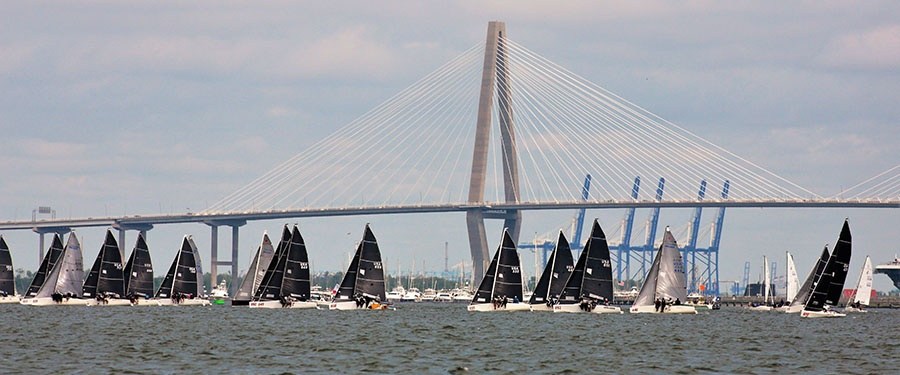 Several sailboats on water with a large bridge in the background.