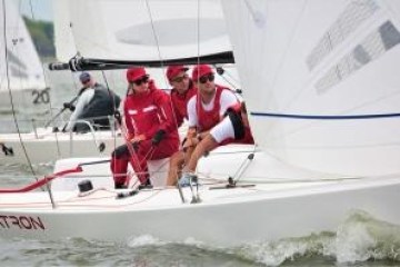 Four sailors in red uniforms on a white sailboat during a race.