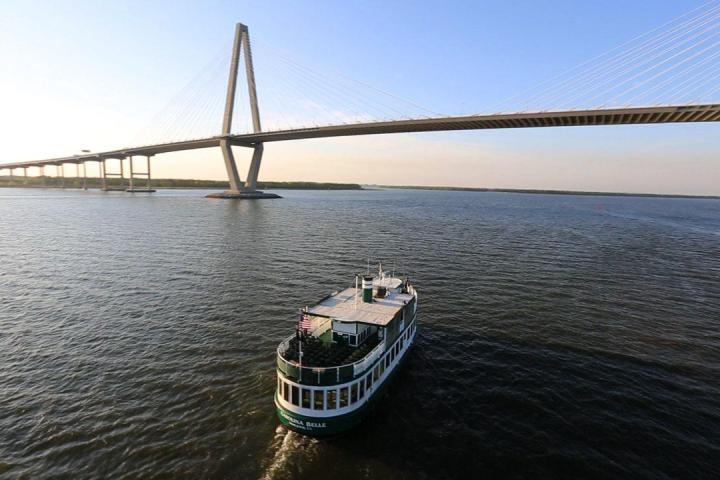 Ferry on wide river under modern cable-stayed bridge at sunset.