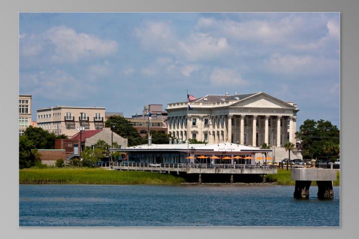 Classic building with columns near waterfront and cityscape under a blue sky.