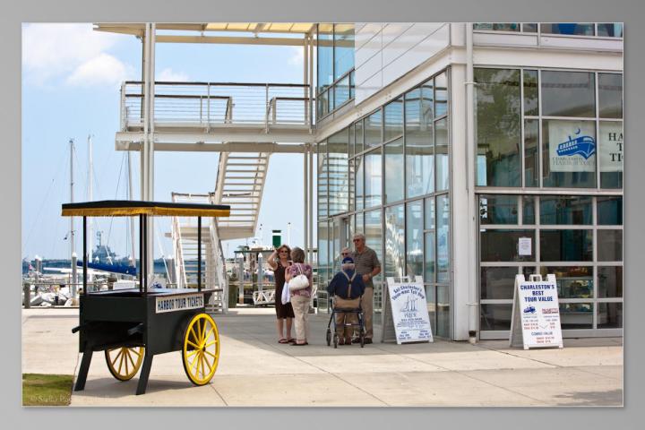 Family near a harbor tours kiosk outside a modern glass building.
