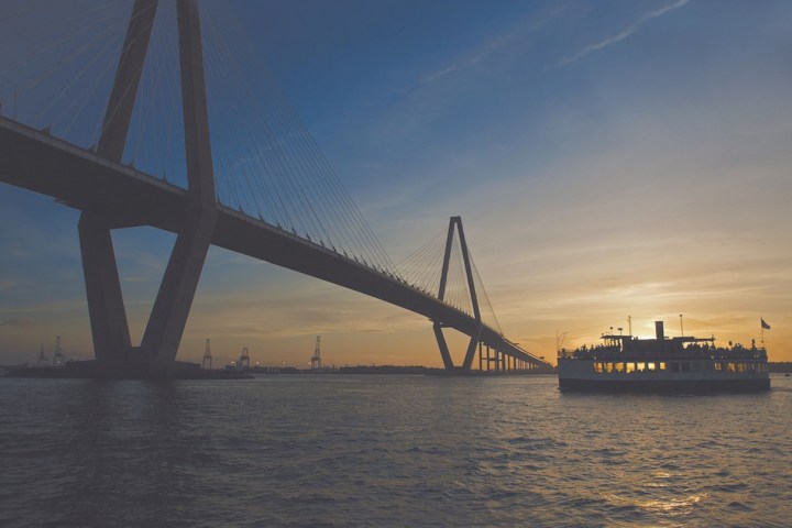 Sunset view of a bridge over water with a ferry passing underneath.