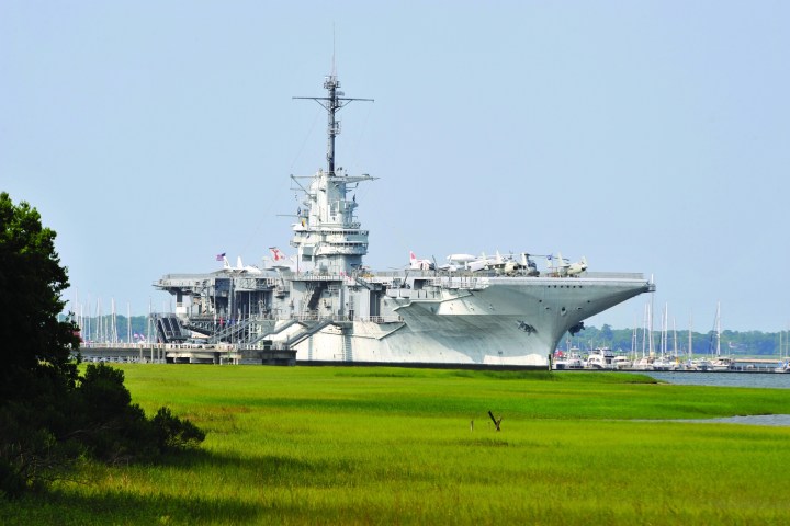 Large aircraft carrier docked near a grassy shoreline.