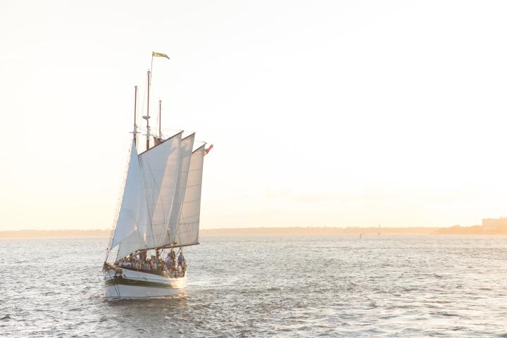 Sailboat on open water during sunset with sails up.