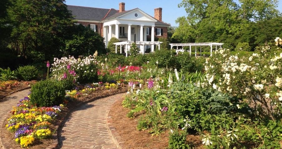 Brick path through colorful garden leading to a white mansion with columns.