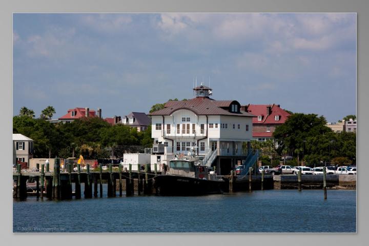 White building on waterfront with docks and boats under a cloudy sky.