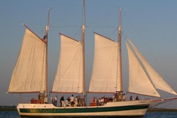 Three-masted schooner sailing on calm water at sunset.