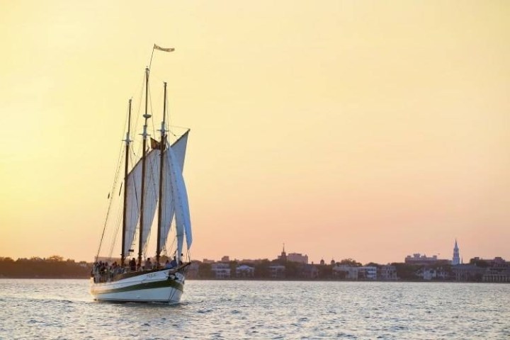 Sailing ship with tall masts on a calm sea at sunset.