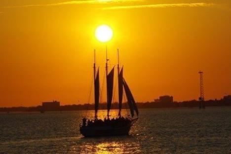 Silhouette of a sailboat at sunset on calm waters.