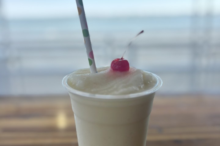 Frozen drink with cherry and straw in foam cup on wooden table.