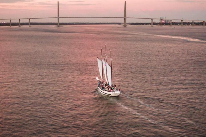 Sailboat on calm water at sunset with a bridge in the background.