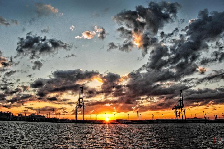 Sunset over water with cranes and dramatic clouds.