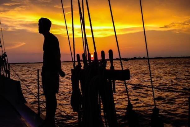Silhouetted person on boat at sunset over calm water.