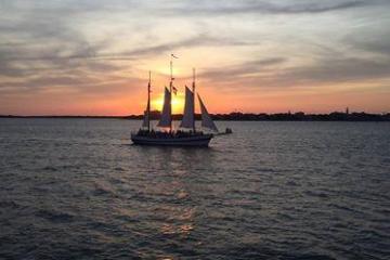 Sailboat on water at sunset with colorful sky and distant shoreline.