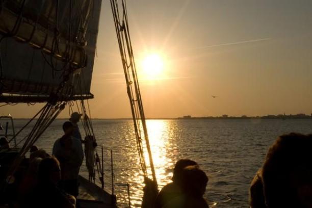 Silhouetted people on a boat at sunset over calm water.