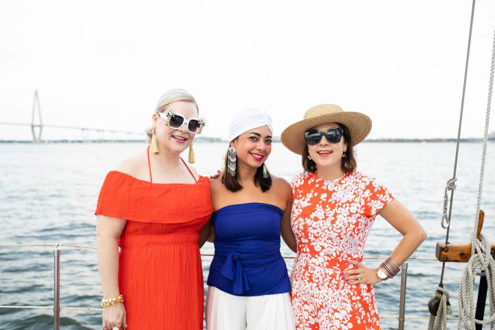 Three women posing on a boat, wearing summer dresses and hats.