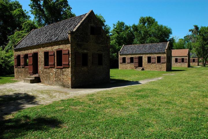 Two historic brick houses with shuttered windows on a grassy field.