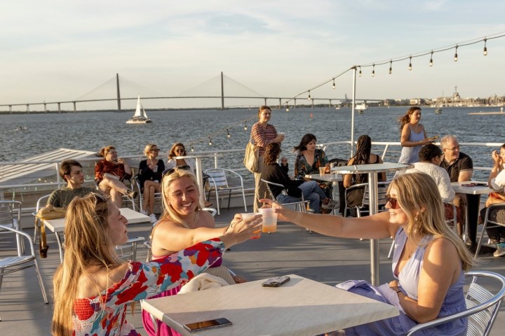 People enjoying drinks on a boat with a bridge in the background.