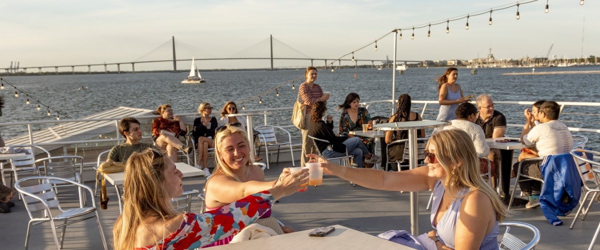 People enjoying drinks on a boat with a bridge in the background.