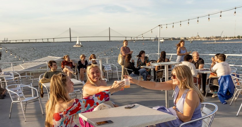 People enjoying drinks on a boat with a bridge in the background.