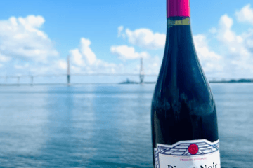 Bottle of Pinot Noir wine by a riverside with a bridge in the background.