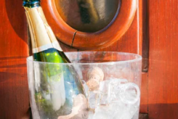 Ice bucket with champagne bottle and small doll inside, against a wooden background.