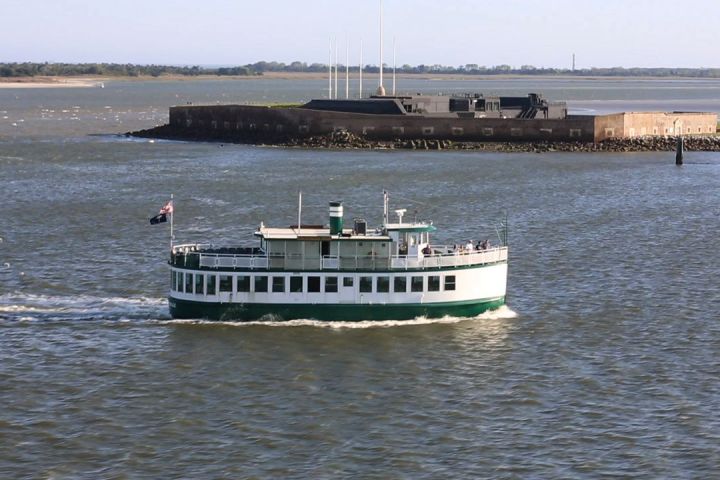 Ferry boat in water near a small fort on a sunny day.