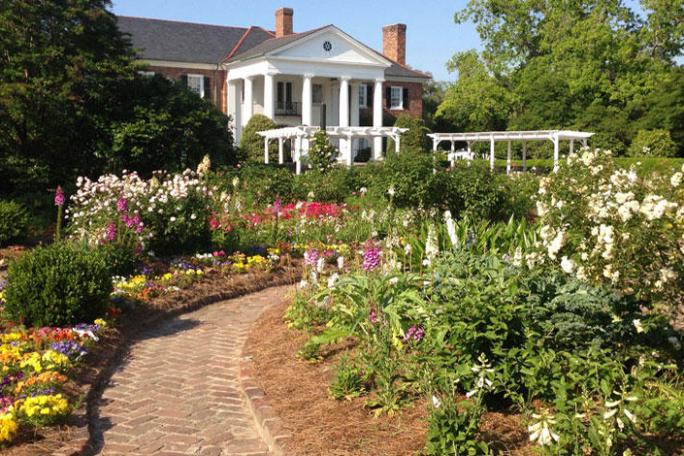 Elegant house with columns and a lush garden path lined with colorful flowers.