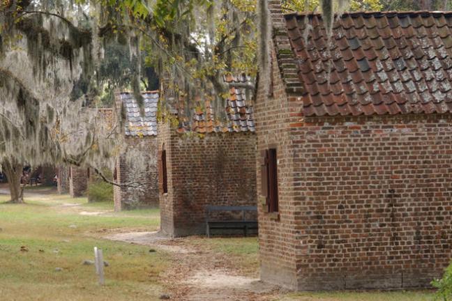 Old brick slave cabins under trees with hanging moss.