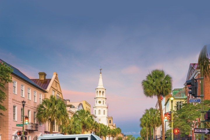 White van on a street with historic buildings and a tall church spire.